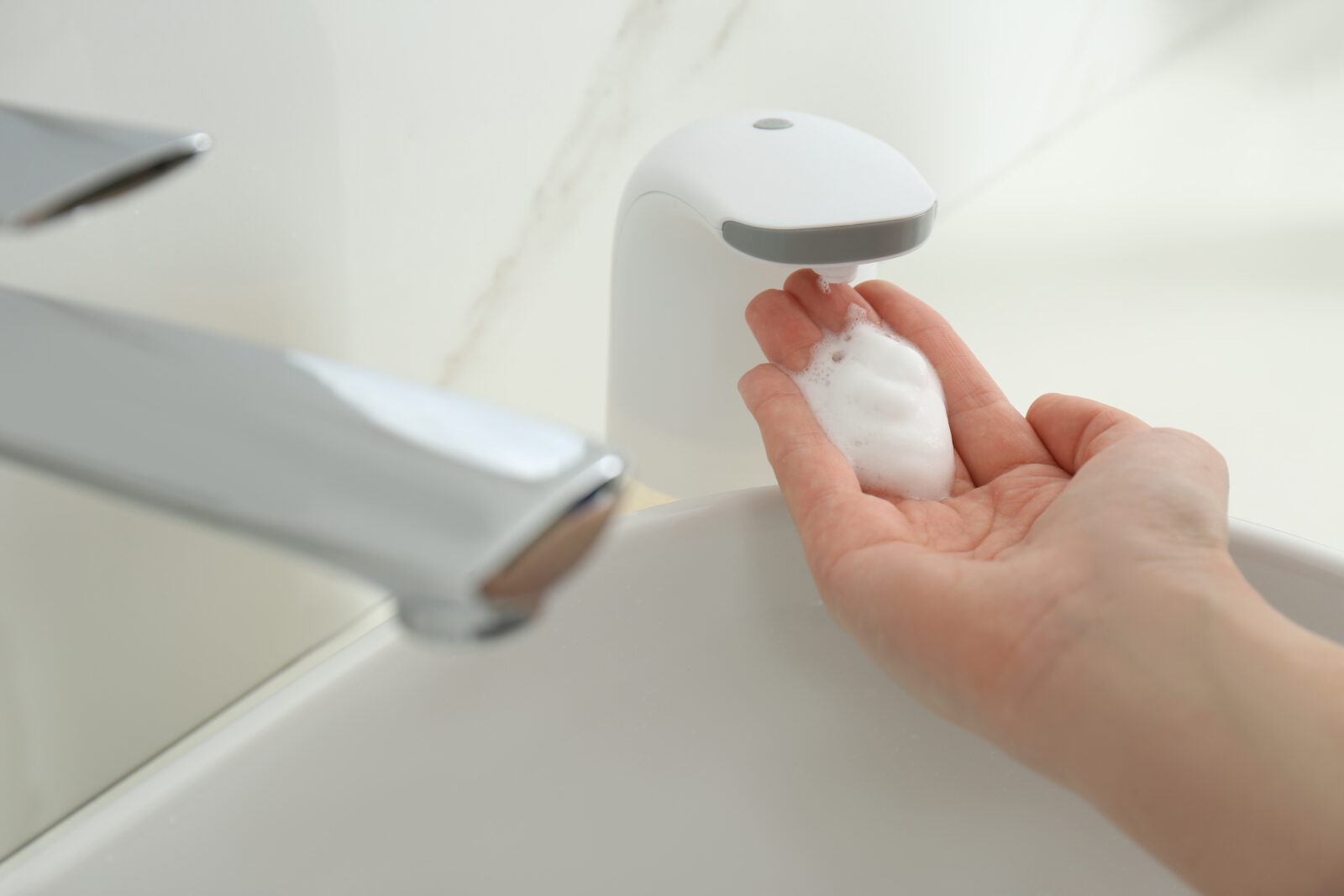 Woman using automatic soap dispenser in bathroom, closeup.