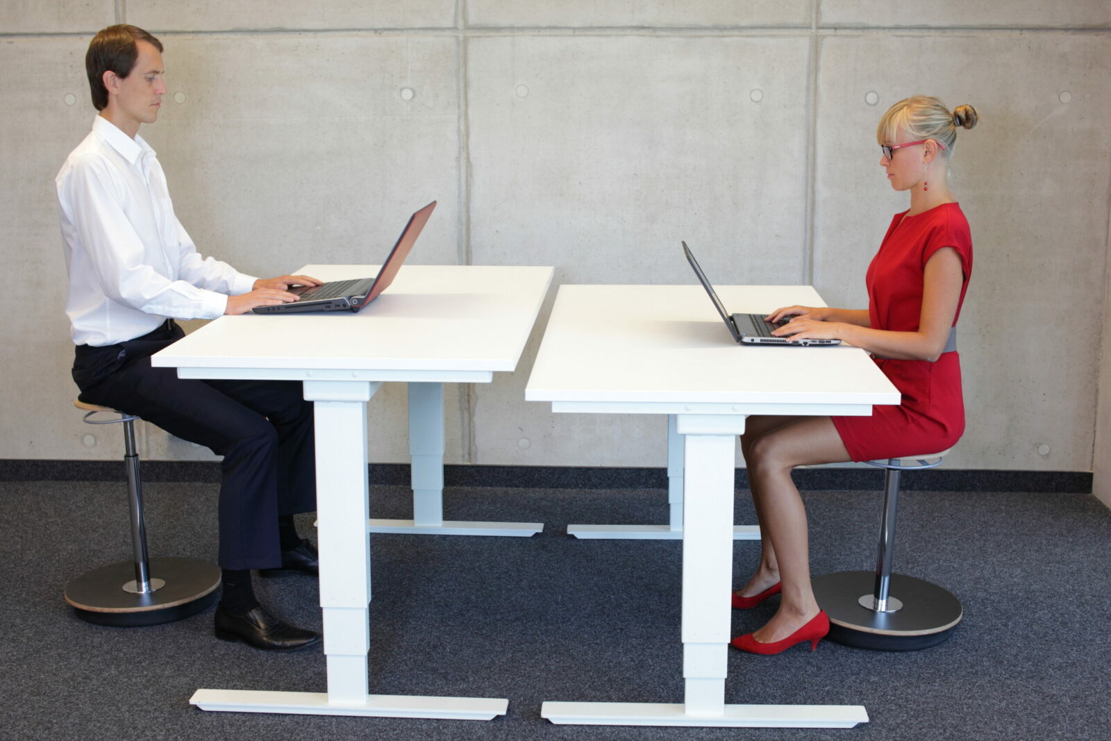 Two coworkers in correct sitting posture at adjustable desks.